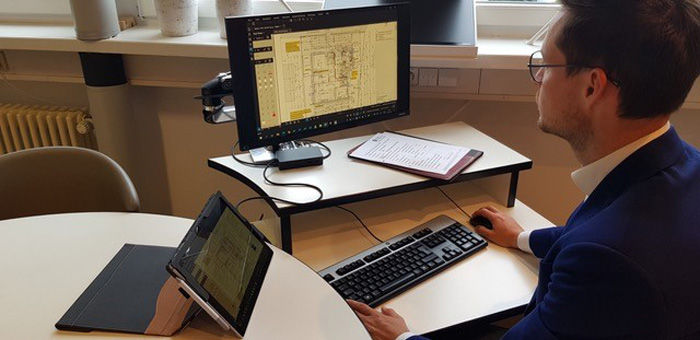 Mann mit Anzug und Brille, der Baupläne auf dem Computer im Büro betrachtet 