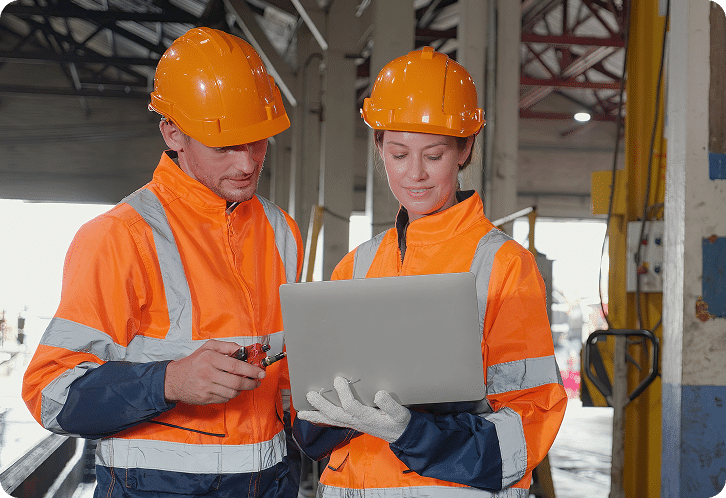 Two construction workers look at laptop onsite.